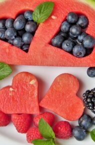 Vari tipi di frutta su un piatto bianco con due pezzi di anguria a forma di cuore