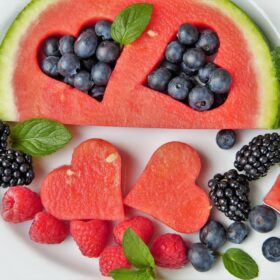 Vari tipi di frutta su un piatto bianco con due pezzi di anguria a forma di cuore