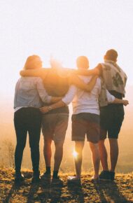 Quattro amici che si stringono a vicenda davanti un tramonto tra le colline