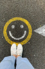 Persona in scarpe bianche in piedi sulla strada di cemento grigia con simbolo del sorriso