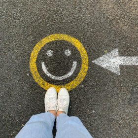 Persona in scarpe bianche in piedi sulla strada di cemento grigia con simbolo del sorriso